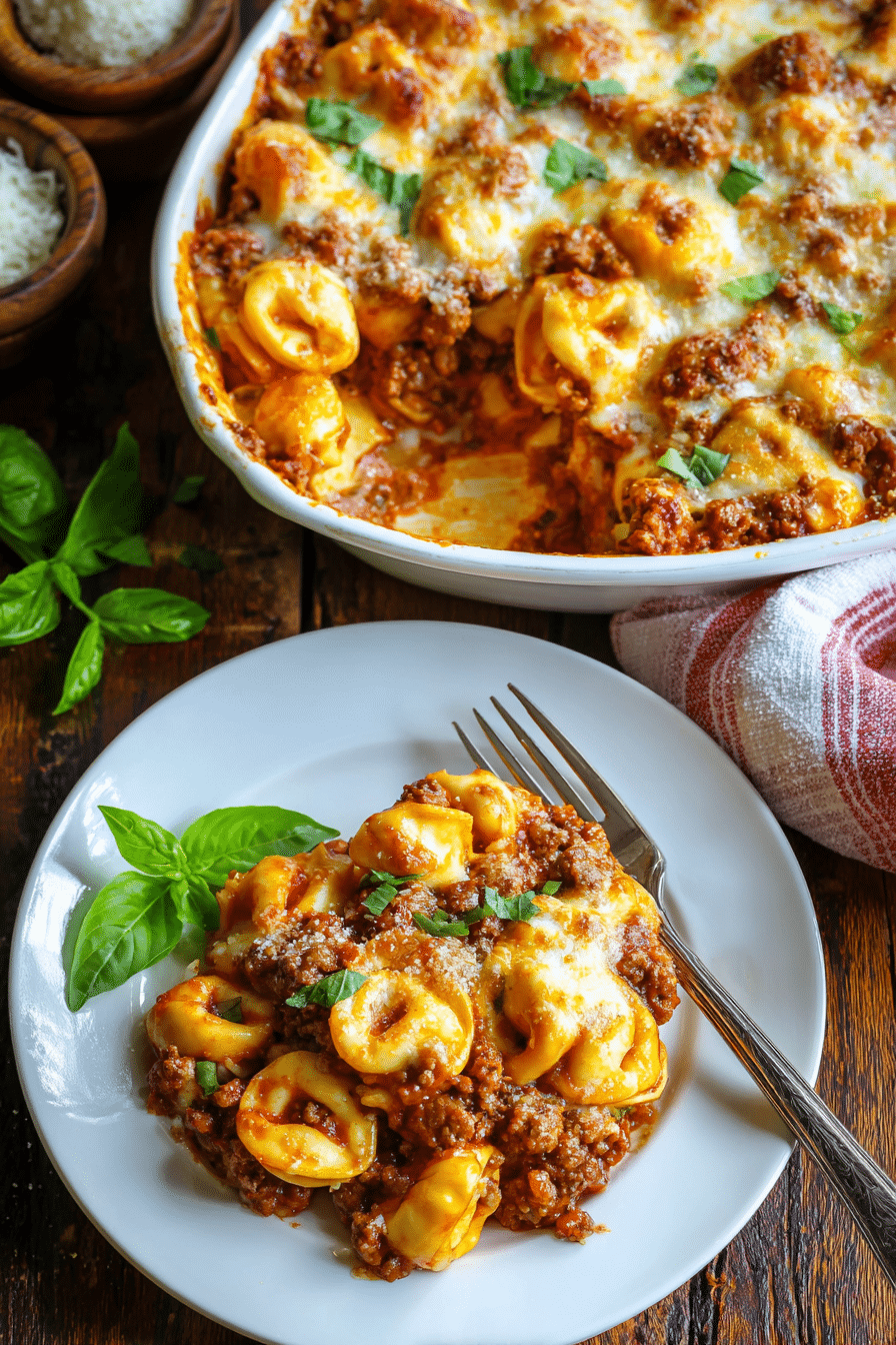 Close-up of beefy tortellini bake in white ceramic dish with melted golden mozzarella and Parmesan cheese, red marinara sauce, tender pasta, and fresh green basil garnish on rustic wooden surface