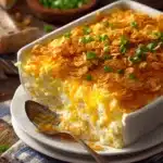 Close-up of a rustic Million Dollar Chicken Casserole in a square dish with creamy shredded chicken, melted cheddar cheese, chopped green onions, and a golden crunchy crust, served on a white plate.