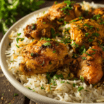 Close-up of one pot shawarma chicken and rice served in a shallow white ceramic bowl, showing tender golden chicken chunks on fluffy long grain rice with visible shawarma spices and fresh parsley garnish on rustic wooden surface