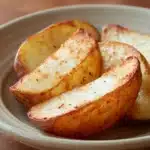 Close-up of crispy air fryer potato halves with golden brown edges on a white plate.