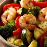 Close-up of air fryer shrimp with colorful vegetables in bright, natural lighting.