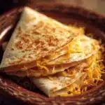 Close-up of a cheesy quesadilla with melted cheese oozing out, on a clean white plate.