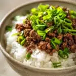 Close-up of a Korean ground beef bowl with rice and vegetables, garnished with sesame seeds.