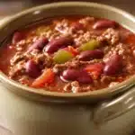 Close-up of a hearty chili soup with beans and tomatoes in a white bowl.