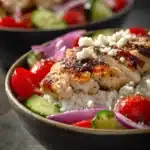 Close-up of Greek chicken bowls with fresh vegetables and herbs.