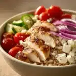 Close-up of Greek chicken rice bowl with cucumber, rice, and herbs in a white bowl.