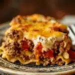 Close-up of a ground beef casserole with egg noodles, topped with melted cheese and herbs.