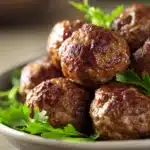 Close-up of Marry Me Meatballs in creamy sauce with herbs on a clean white plate.