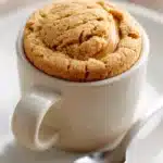Close-up of a peanut butter cookie in a cup with warm lighting and minimal background.