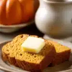 Close-up of pumpkin bread with butter on a clean background, highlighting textures and warm tones.