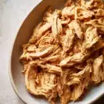 Close-up of shredded chicken meal prep with bright natural lighting and minimal background.