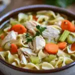 Close-up of slow cooker chicken noodle soup with noodles, chicken, and vegetables in a bowl.