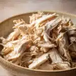 Close-up of slow cooker chicken shredded with creamy sauce on a white plate
