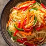 Close-up of spicy noodles with vibrant colors and garnishes, perfect for a flavorful meal.