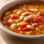 Close-up of Tuscan White Bean Soup with herbs in a bright, warm setting.