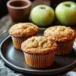 Close-up of apple muffin with fresh apples, showcasing appetizing textures and warm lighting.