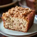 Close-up of banana bread coffee cake with a crumbly topping on a white plate.