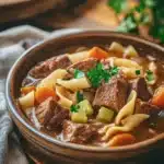Close-up of beef stew and noodles in a crock pot with bright lighting and minimal background.