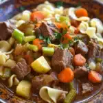 Close-up of beef stew and noodles in a crock pot with rich sauce and vegetables.
