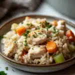 Close-up of a chicken and rice casserole with a golden crust, served in a white dish.