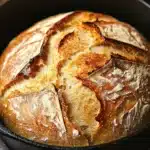 Close-up of a golden-brown no knead bread in a cast iron dutch oven