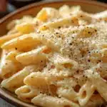 Close-up of creamy garlic cheese pasta in a white bowl with parsley garnish