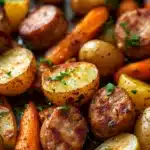 Close-up of sheet pan with sausage, potatoes, and carrots in bright natural light