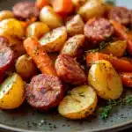 Sheet pan with roasted sausage, potatoes, and carrots in a bright, appetizing close-up.