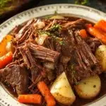 Close-up of slow cooker pot roast with ranch dressing, garnished with herbs.