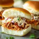 Close-up of slow cooker zesty BBQ chicken sliders with a creamy sauce on a clean background.