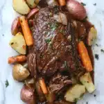 3 packet pot roast slow cooker - the image shows a plate of cooked beef stew with potatoes and carrots. the beef is cooked medium-rare and has a rich, dark brown color. the potatoes are cut into small cubes and are arranged in a pile on top of the beef. the carrots are bright orange and are scattered around the plate. the dish is garnished with chopped parsley. the plate is white and the background is a marble countertop.