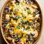 Baked chicken and wild rice casserole - the image shows a casserole dish filled with a dish of chicken and rice. the dish is made of ceramic and is placed on a wooden table. the chicken is cooked to a golden brown color and is topped with melted cheese and sliced mushrooms. the rice is a mix of brown and white colors, and there are a few sprigs of fresh parsley scattered around the dish. the overall appearance of the dish is savory and appetizing.
