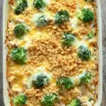 Cheesy rotisserie chicken broccoli rice casserole - the image shows a white rectangular baking dish filled with a casserole dish. the dish appears to be made with broccoli, cheese, and crumbled breadcrumbs. the broccoli is cut into small pieces and is arranged in a circular pattern on top of the cheese. the cheese is melted and bubbly, and there are small chunks of broccoli scattered throughout the dish. there are also some crumbs on top, indicating that the dish has been baked. the baking dish is sitting on a wooden table.