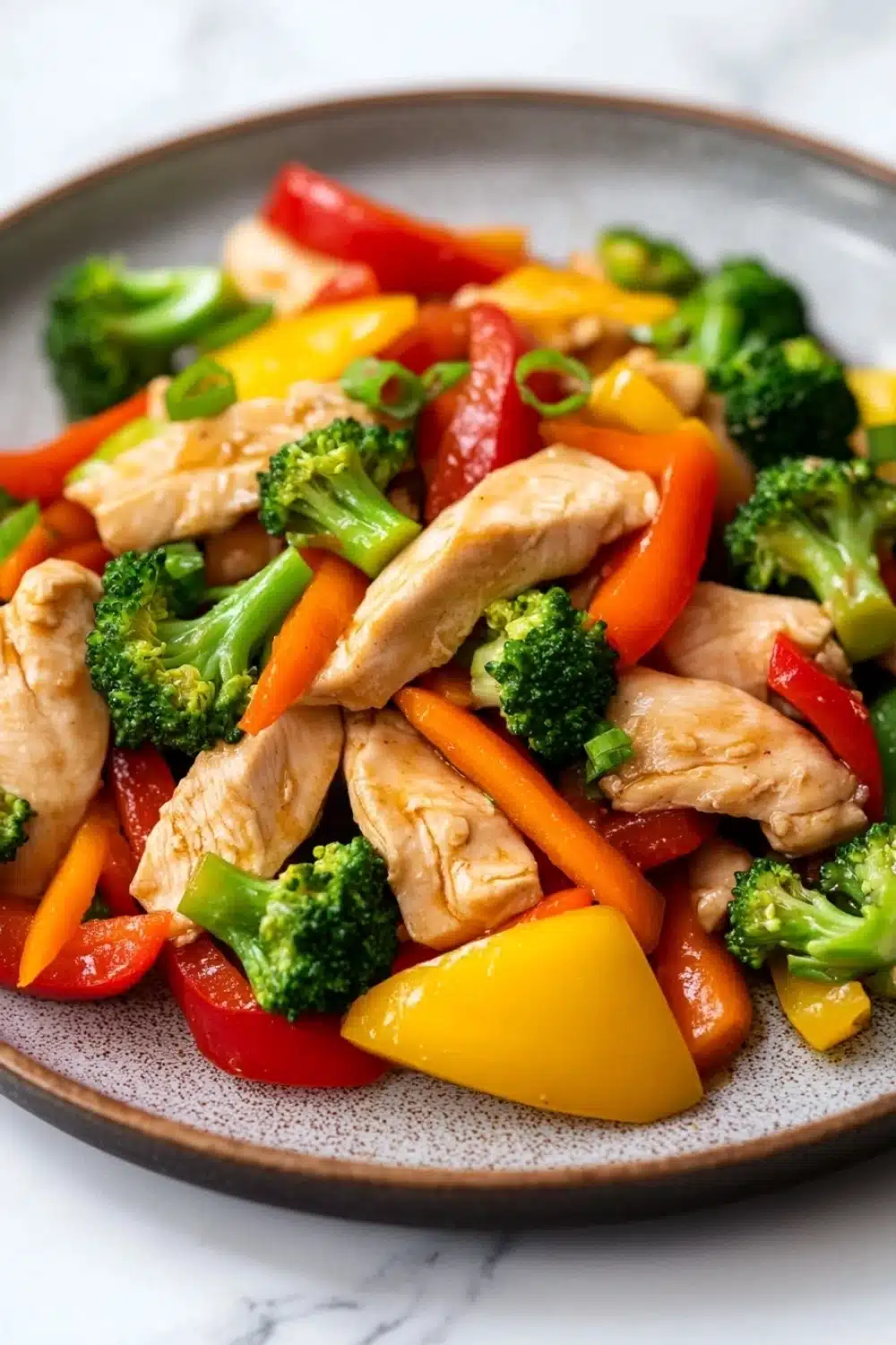 Chicken breast stir fry - the image is a close-up of a plate of stir-fry with chicken and vegetables. the plate is round and has a light brown color with a speckled pattern. the chicken is cut into small pieces and is mixed with various vegetables such as broccoli, red and yellow bell peppers, and orange carrots. the vegetables are cut into thin strips and are arranged in a colorful and appetizing manner. the dish appears to be freshly cooked and ready to eat.