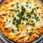 Crock pot buffalo chicken dip - the image is a close-up of a round pizza on a gray plate. the pizza has a golden-brown crust and is topped with melted cheese and chopped green onions. the cheese appears to be melted and bubbly, and the onions are bright green. the plate is sitting on a white marble countertop.