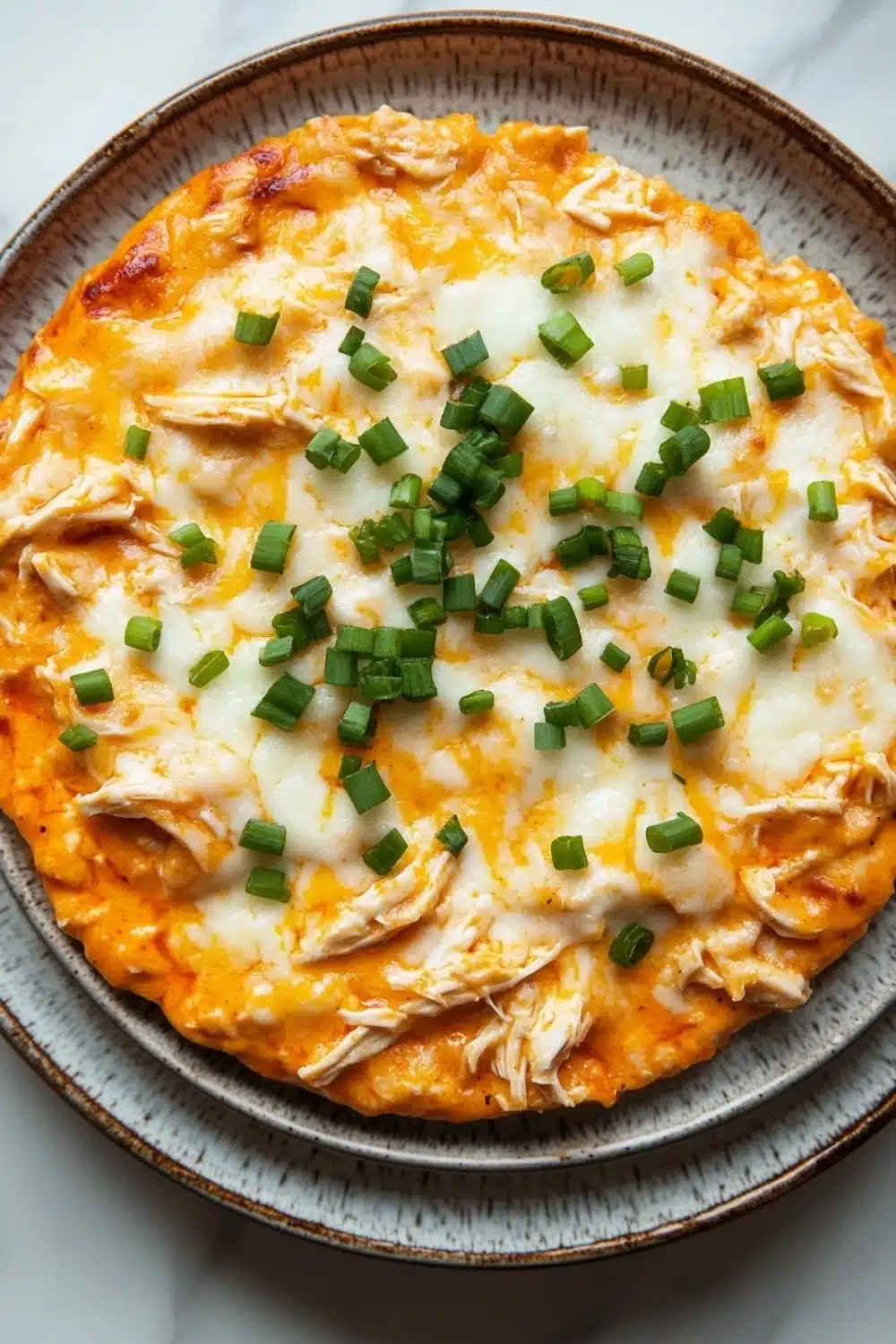 Crock pot buffalo chicken dip - the image is a close-up of a round pizza on a gray plate. the pizza has a golden-brown crust and is topped with melted cheese and chopped green onions. the cheese appears to be melted and bubbly, and the onions are bright green. the plate is sitting on a white marble countertop.