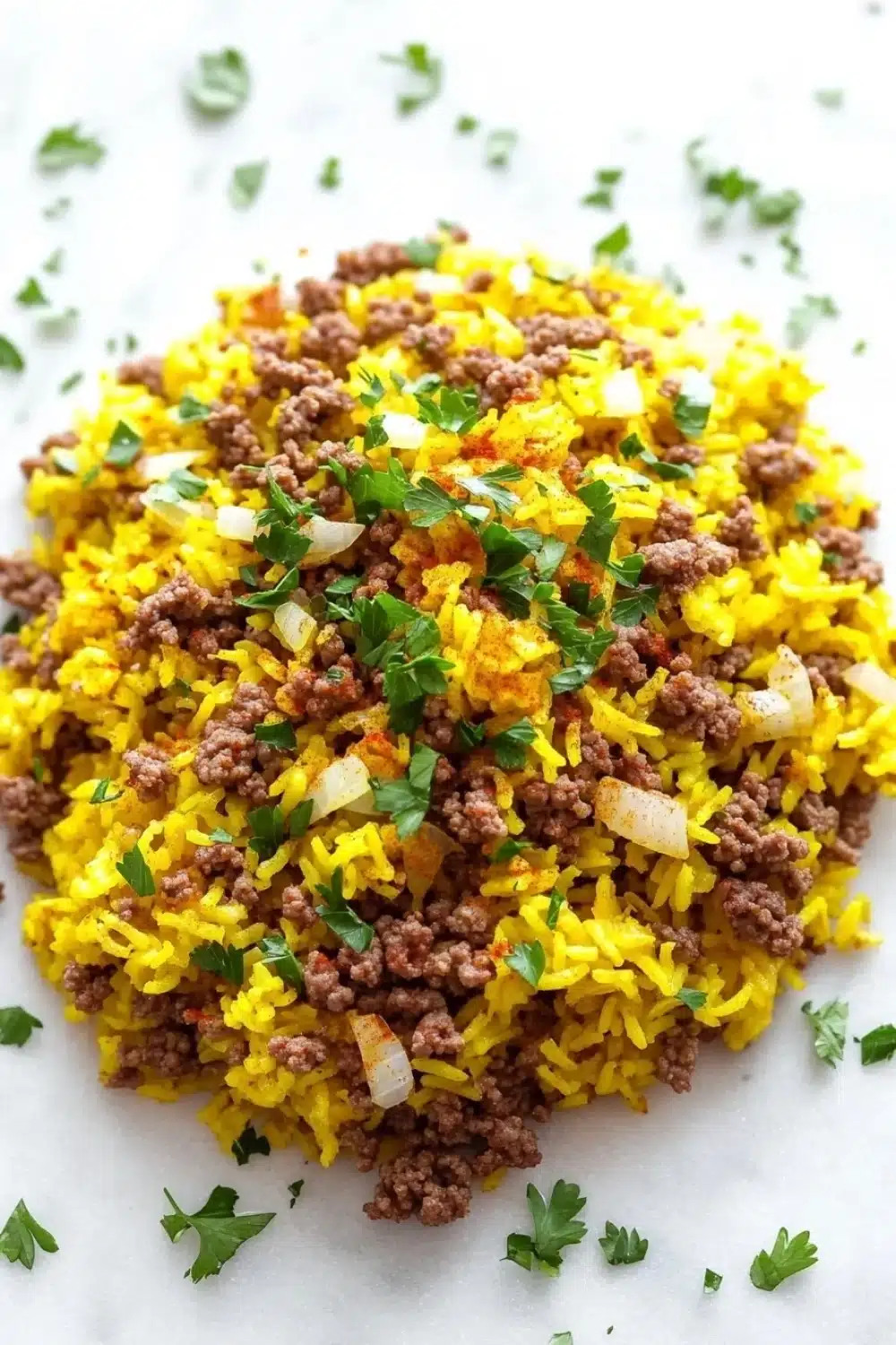 Ground beef and yellow rice for dinner - the image shows a close-up of a dish made with yellow rice and ground beef. the rice appears to be cooked and has a golden-brown color. the ground beef is scattered throughout the dish, with some pieces of diced onions and chopped parsley scattered around it. the dish is served on a white parchment paper. the background is blurred, making the dish the focal point of the image.