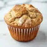 Kodiak muffin mix with yogurt - the image is of a freshly baked muffin on a white marble surface. the muffin is golden brown in color and has a crumbly texture on top. it appears to be a muffin with a soft, fluffy interior. the edges of the muffin are lined with white paper liners. the background is blurred, making the muffins the focal point of the image.