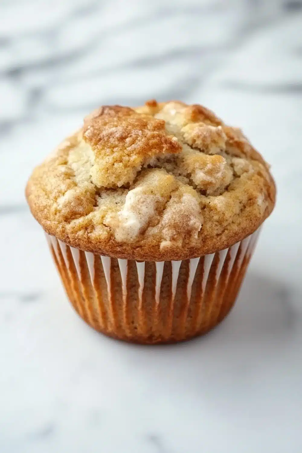 Kodiak muffin mix with yogurt - the image is of a freshly baked muffin on a white marble surface. the muffin is golden brown in color and has a crumbly texture on top. it appears to be a muffin with a soft, fluffy interior. the edges of the muffin are lined with white paper liners. the background is blurred, making the muffins the focal point of the image.