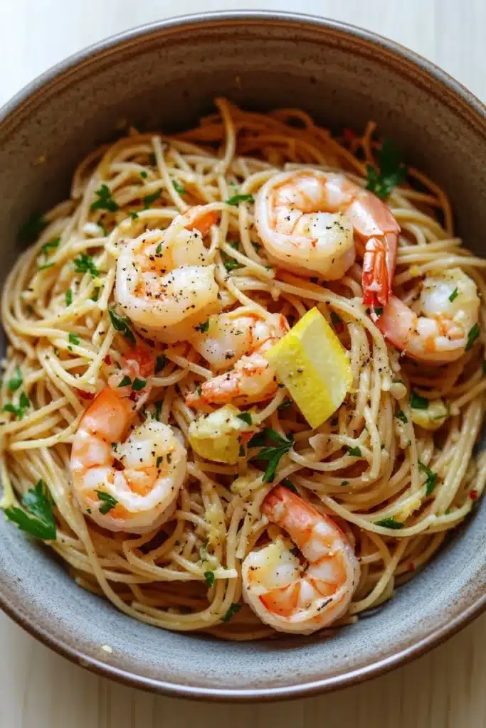 Low calorie shrimp scampi pasta - the image is a close-up of a bowl of spaghetti with shrimp and lemon wedges. the spaghetti is cooked al dente and is garnished with chopped parsley. the shrimp are large and pink, and they are arranged in a circular pattern on top of the spaghetti. the dish is served in a light brown bowl with a textured surface. the background is a wooden table.