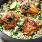 One pot cilantro lime chicken and rice - the image shows a large black skillet filled with a dish of rice and chicken. the rice is white and fluffy, and the chicken is cooked to a golden brown color. the dish is garnished with fresh cilantro and a lime wedge. the skillet is sitting on a wooden cutting board, and there is a white countertop in the background. the overall color scheme of the dish is warm and inviting.