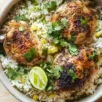 One pot cilantro lime chicken and rice - the image shows a bowl of rice with two pieces of grilled chicken on top. the chicken is golden brown and appears to be seasoned with herbs and spices. the rice is white and fluffy, and there are small pieces of corn scattered throughout the dish. a lime wedge is placed on top of the rice, adding a pop of green color to the dish and garnished with fresh cilantro. the bowl is sitting on a wooden cutting board.