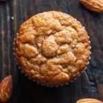 Protein muffin almond flour - the image is a close-up of a freshly baked muffin on a dark wooden surface. the muffin is round and has a golden brown color with a crumbly texture. it is topped with a sprinkle of powdered sugar, giving it a shiny appearance. around the muffin, there are several whole almonds scattered around, adding a pop of color to the image. the background is blurred, making the focus of the image the main focus.