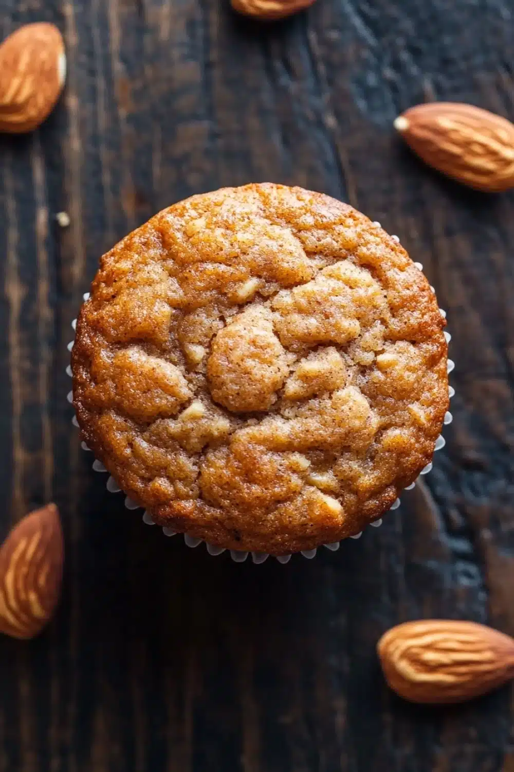 Protein muffin almond flour - the image is a close-up of a freshly baked muffin on a dark wooden surface. the muffin is round and has a golden brown color with a crumbly texture. it is topped with a sprinkle of powdered sugar, giving it a shiny appearance. around the muffin, there are several whole almonds scattered around, adding a pop of color to the image. the background is blurred, making the focus of the image the main focus.