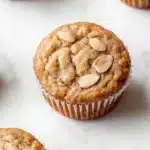 Protein muffin almond flour - the image shows a group of freshly baked muffins on a white marble surface. the muffins are golden brown in color and have a crumbly texture. they are topped with sliced almonds, giving them a crunchy appearance. the background is blurred, making the muffins the focal point of the image.