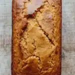 Pumpkin bread almond flour - the image is a close-up of a freshly baked loaf of bread. the bread appears to be golden brown in color and has a crumbly texture. it is sitting on a wooden surface with a textured surface. the loaf is rectangular in shape and is slightly tilted to the side. the edges of the bread are slightly frayed, indicating that it has been freshly baked. the background is blurred, making the bread the focal point of the image.