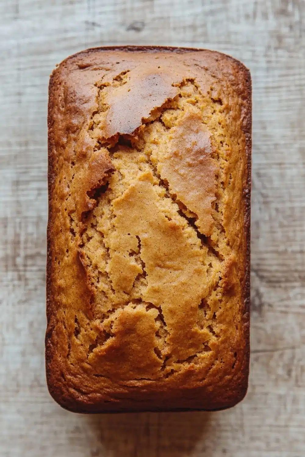 Pumpkin bread almond flour - the image is a close-up of a freshly baked loaf of bread. the bread appears to be golden brown in color and has a crumbly texture. it is sitting on a wooden surface with a textured surface. the loaf is rectangular in shape and is slightly tilted to the side. the edges of the bread are slightly frayed, indicating that it has been freshly baked. the background is blurred, making the bread the focal point of the image.