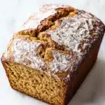 Pumpkin bread almond flour - the image is a close-up of a freshly baked loaf of bread. the bread appears to be golden brown in color and has a slightly crumbly texture. it is dusted with a light dusting of powdered sugar, giving it a shiny appearance. the loaf is sitting on a white marble countertop. the background is blurred, making the bread the focal point of the image.