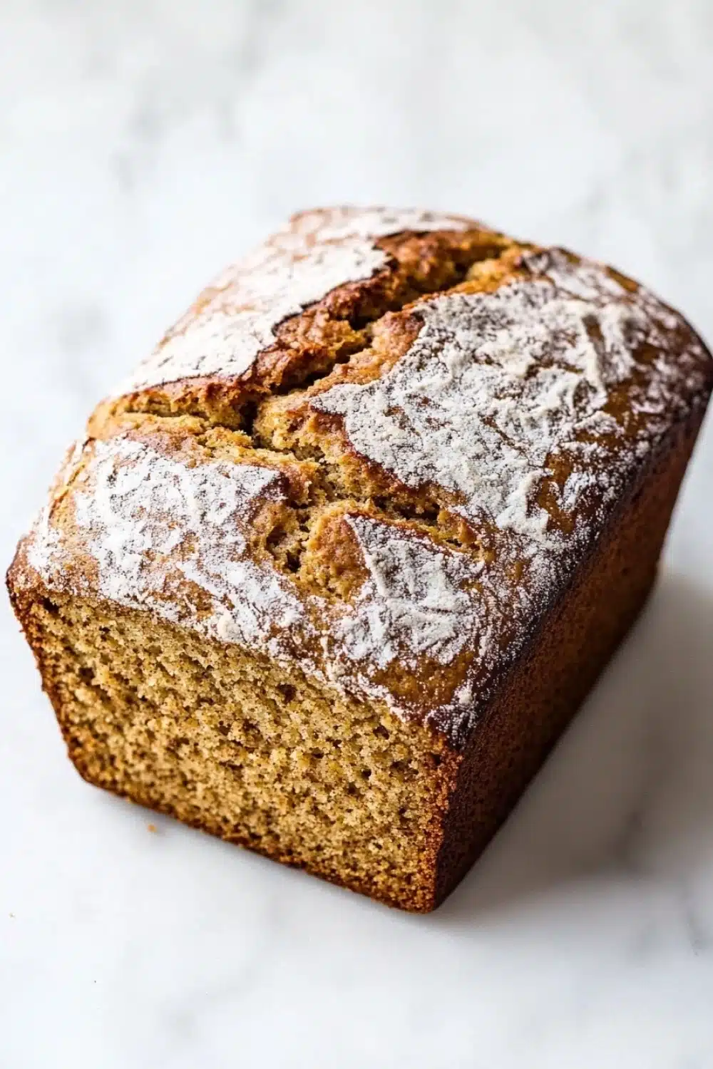 Pumpkin bread almond flour - the image is a close-up of a freshly baked loaf of bread. the bread appears to be golden brown in color and has a slightly crumbly texture. it is dusted with a light dusting of powdered sugar, giving it a shiny appearance. the loaf is sitting on a white marble countertop. the background is blurred, making the bread the focal point of the image.