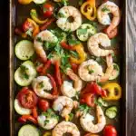 Shrimp sheet pan - the image shows a rectangular baking tray filled with cooked shrimp and vegetables. the shrimp are arranged in a circular pattern on the tray, with some overlapping each other. the vegetables include sliced zucchini, cherry tomatoes, yellow bell peppers, and red bell peppers. there are also some herbs sprinkled on top, adding a pop of green color to the dish. the tray is placed on a wooden table, and the background is blurred, making the colors of the vegetables stand out.